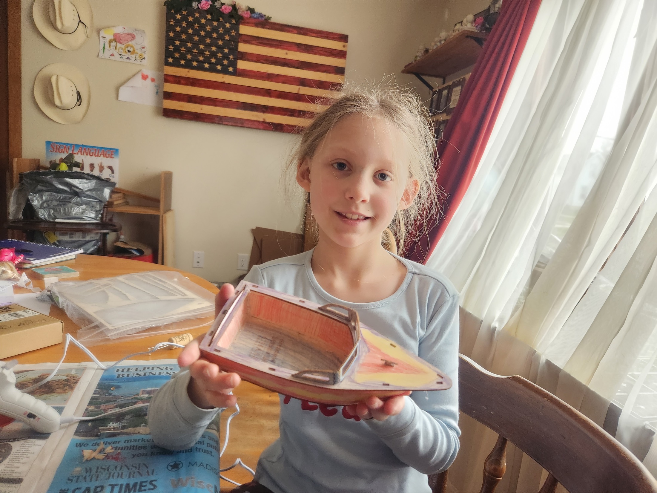 A young learner proudly holding a completed wooden boat model at home
