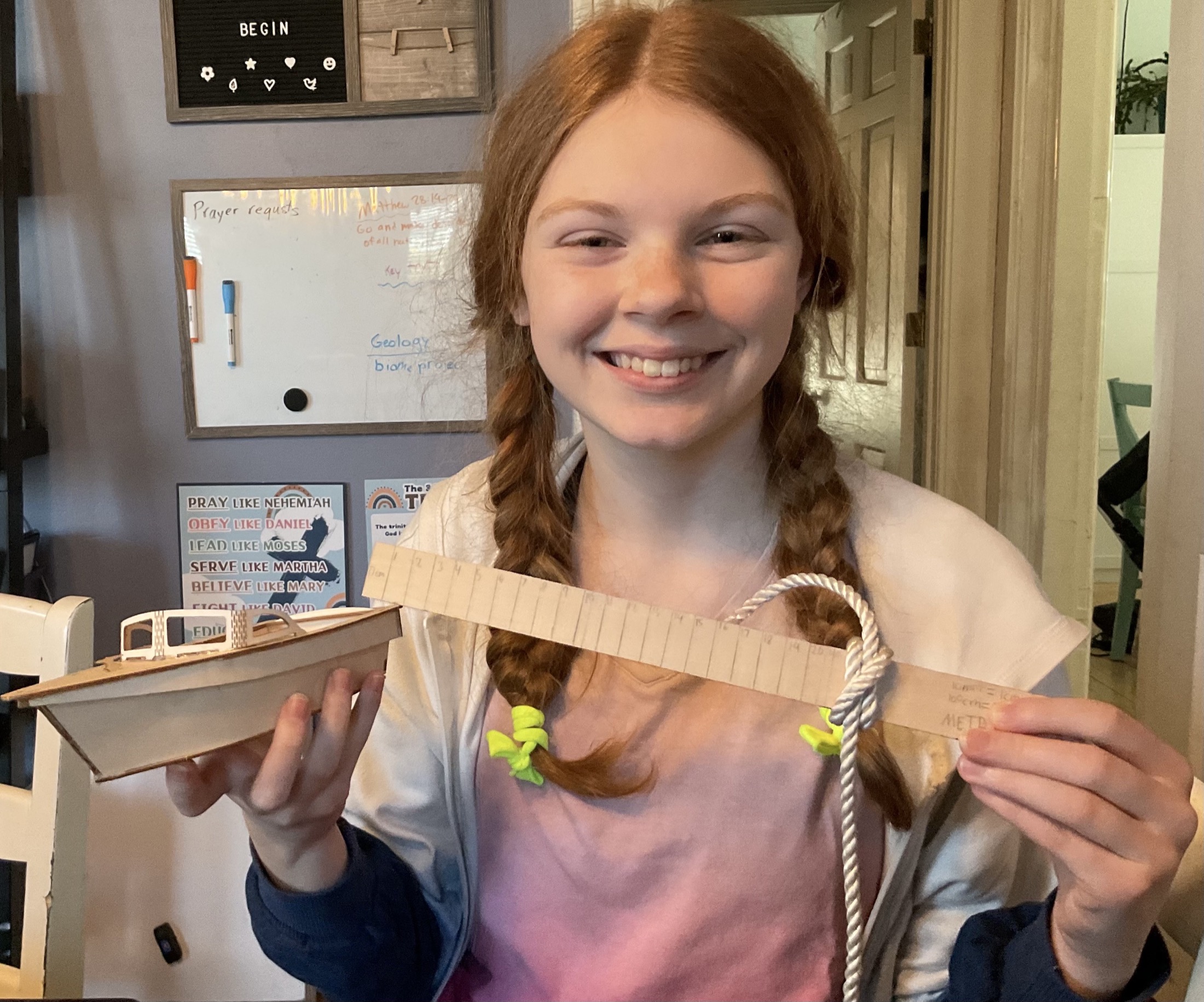 A learner displaying a completed boat model, measuring tool, and knot during a skill assessment